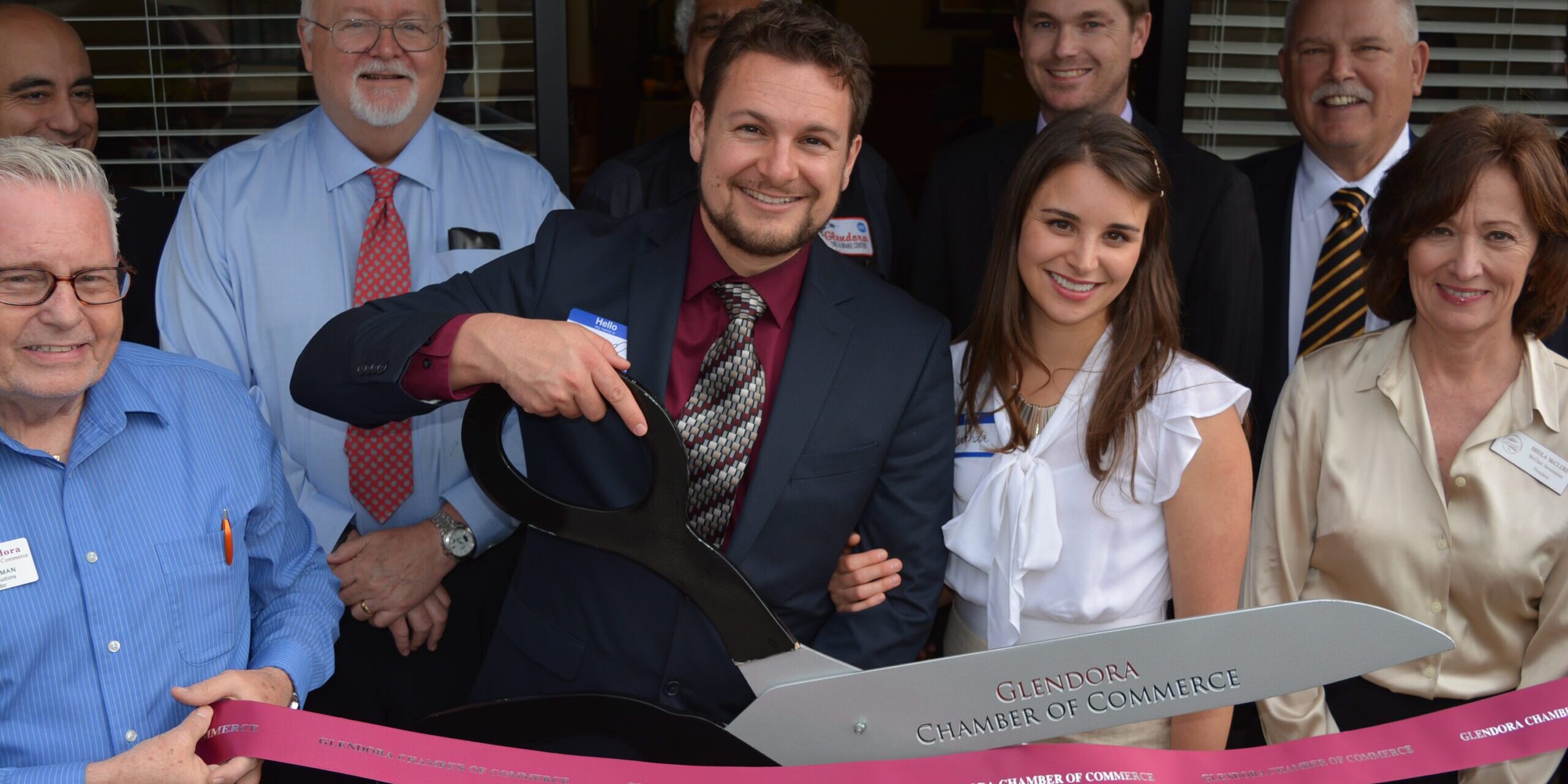 Merrill A. Hanson, wife, and people in front of Merrill's office cutting a ribbon.