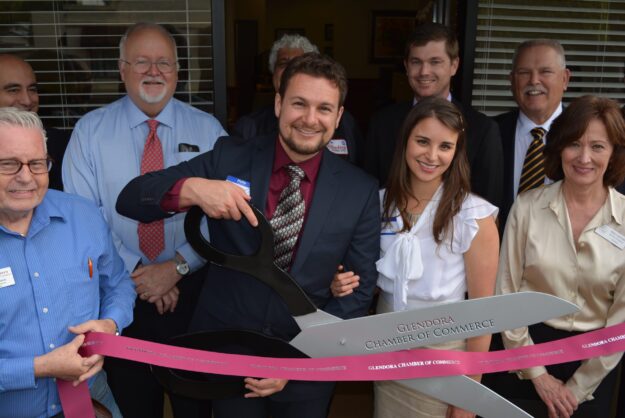 Merrill A. Hanson, wife, and people in front of Merrill's office cutting a ribbon.