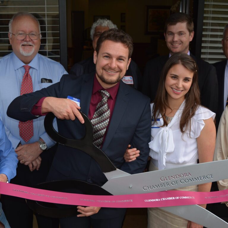 Merrill A. Hanson, wife, and people in front of Merrill's office cutting a ribbon.