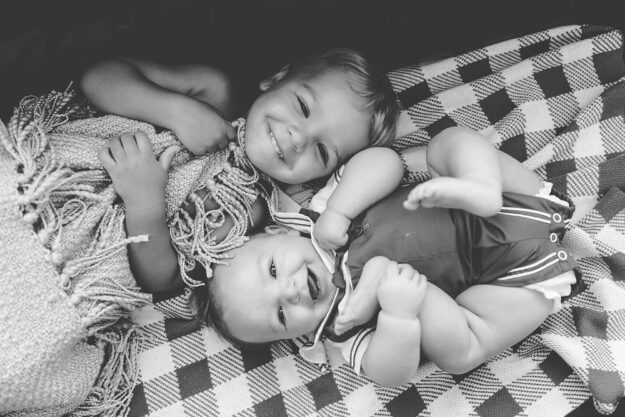 Two babies on a blanket smiling into the camera.