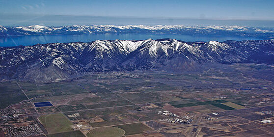 Arial view of snow top mountains, Lake Tahoe and house with fields.