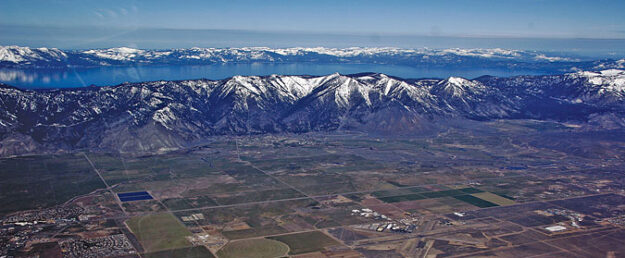 Arial view of snow top mountains, Lake Tahoe and house with fields.