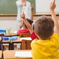 Classroom with children raising their hand with the view from back of room.