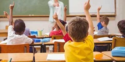 Classroom with children raising their hand with the view from back of room.