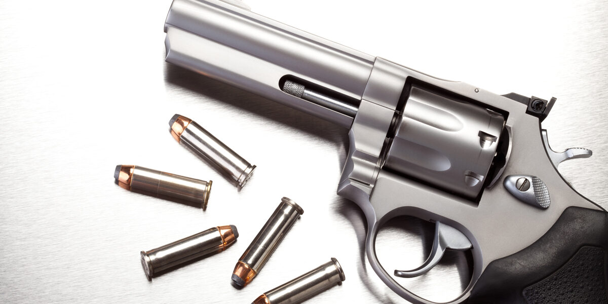 Close up of gun with bullet shells next to it in black and white.