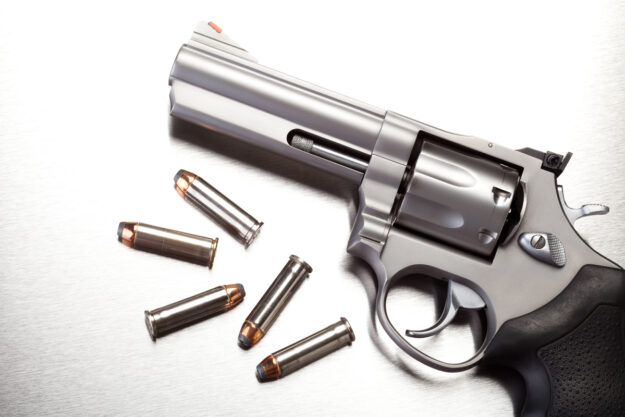 Close up of gun with bullet shells next to it in black and white.