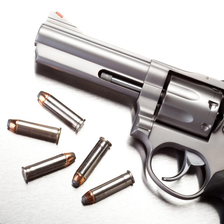 Close up of gun with bullet shells next to it in black and white.