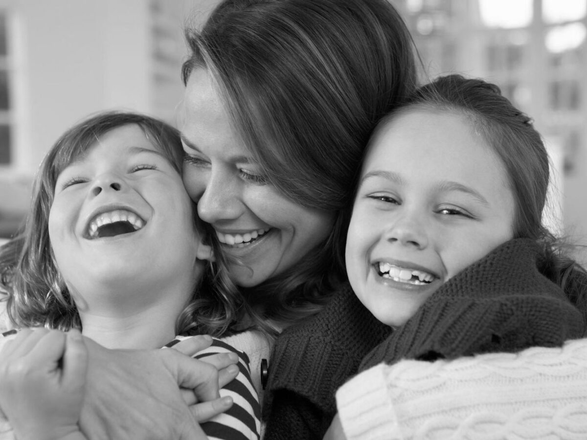 Mother with her arms around her son and daughter laughing.