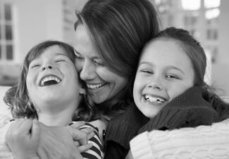 Mother with her arms around her son and daughter laughing.