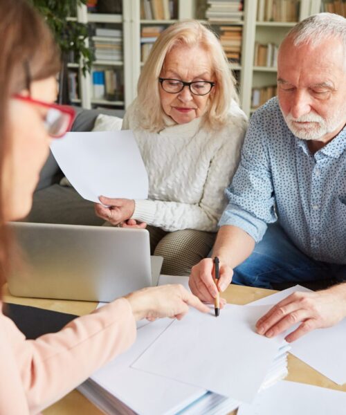 An elderly couple sign documents with a lady associate.